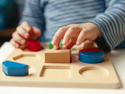 Educational toys, Cognitive skills, Montessori activity. Closeup: Hands of a little Montessori kid learning about color, shape, sorting, arranging by engaged colorful wooden sensorial blocks. — Photo by Deposit Photos