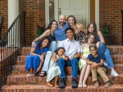 A large and blended and mixed happy family sitting on the front steps of their brick home in the suburbs. — Photo ucpage/Deposit photos