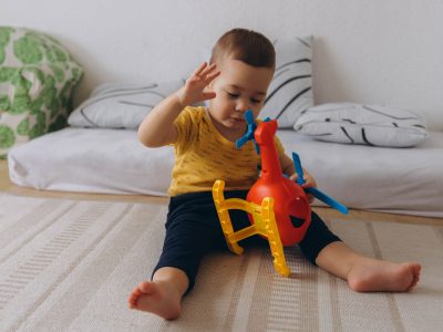 Baby sitting on the floor, playing with a red helicopter, enjoying a moment of fun and discovery (image courtesy Deposit Photos)